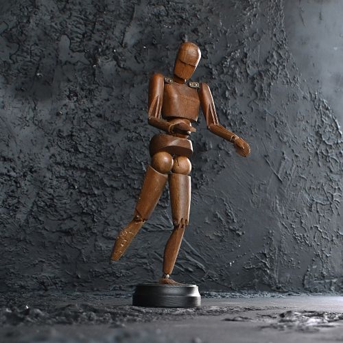 fig 1. An articulated wooden lay figure with carved facial details and metal shoulder joints, standing on a circular dark base.