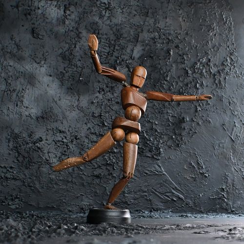 fig 2. An articulated wooden lay figure with carved facial details and metal shoulder joints, standing on a circular dark base.
