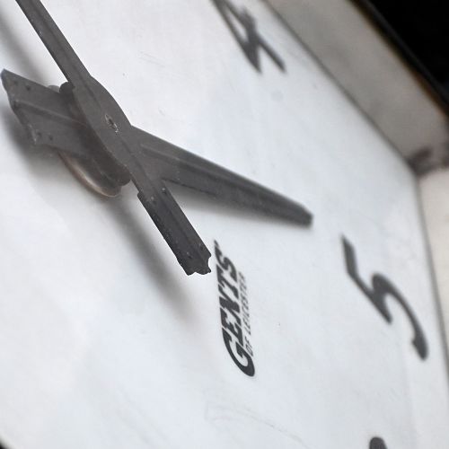 fig 3. A square black steel Gents of Leicester station clock featuring a white face with bold black Arabic numerals and metal mounting feet.
