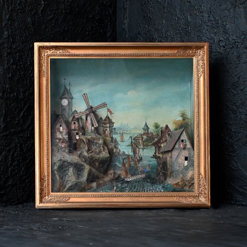 fig 1. A nineteenth-century framed picture clock shadowbox featuring a painted coastal village scene with a windmill, clock tower, and sailing vessels inside a gilt frame.