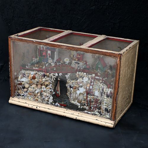 fig 2. An early 20th-century glazed wooden shadow box containing a miniature seaside village diorama constructed from natural sea shells, painted miniature houses, a red bridge, and small figurines.
