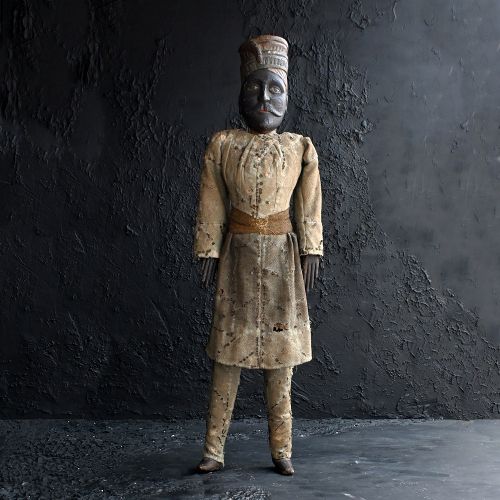 fig 1. A 19th-century Sicilian hand-carved wooden marionette puppet in a seated position, wearing a sequined off-white tunic and tall cylindrical hat with dark painted facial features.