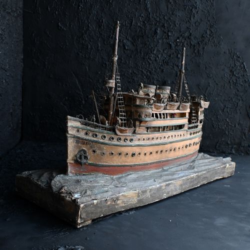 fig 1. A handcrafted wooden folk art steamship model with twin masts and painted hull details mounted on a carved base representing sea waves.