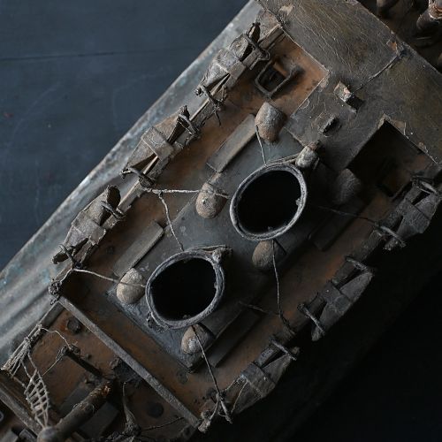 fig 2. A handcrafted wooden folk art steamship model with twin masts and painted hull details mounted on a carved base representing sea waves.