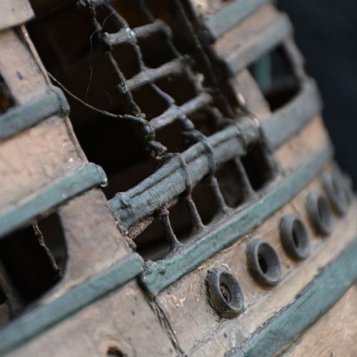 fig 3. A handcrafted wooden folk art steamship model with twin masts and painted hull details mounted on a carved base representing sea waves.