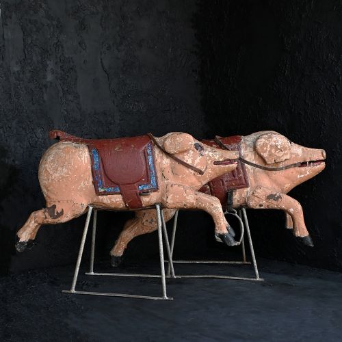 fig 1. A pair of 19th-century carved wooden carousel pigs with distressed pink paint mounted on slender iron display stands.