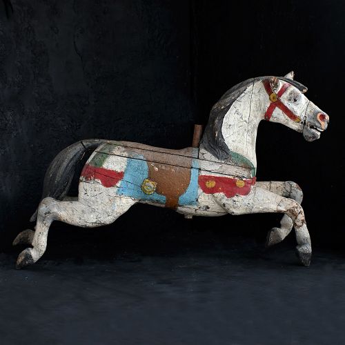 fig 1. A 19th-century French carved wooden carousel horse with distressed white, red, green, and blue paint in a galloping pose.