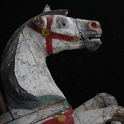 fig 3. A 19th-century French carved wooden carousel horse with distressed white, red, green, and blue paint in a galloping pose.