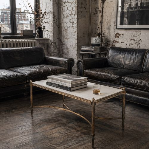 fig 1. A rectangular Neoclassical style coffee table featuring a cream marble surface, a gilt brass frame with fluted legs, corner pineapple finials, and a curved stretcher.