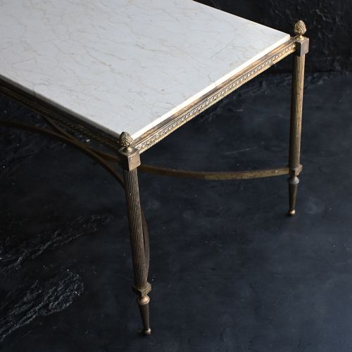 fig 3. A rectangular Neoclassical style coffee table featuring a cream marble surface, a gilt brass frame with fluted legs, corner pineapple finials, and a curved stretcher.