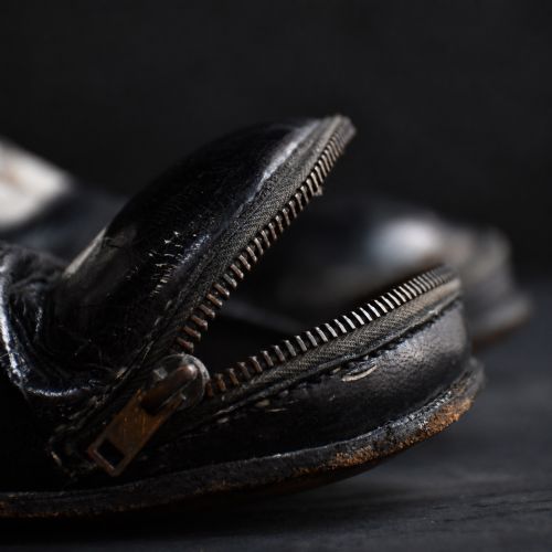 fig 1. A pair of early 20th-century black and white leather clown boots featuring exaggerated toe boxes, lace-up fronts, buckled straps, toe zippers, and fitted wooden boot stretchers.