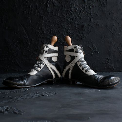 fig 5. A pair of early 20th-century black and white leather clown boots featuring exaggerated toe boxes, lace-up fronts, buckled straps, toe zippers, and fitted wooden boot stretchers.
