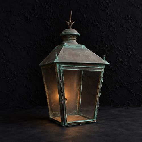 fig 1. A nineteenth-century copper wall lantern with glazed panels, a tapered rectangular body, and a decorative finial on top.