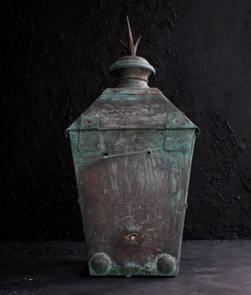 fig 5. A nineteenth-century copper wall lantern with glazed panels, a tapered rectangular body, and a decorative finial on top.