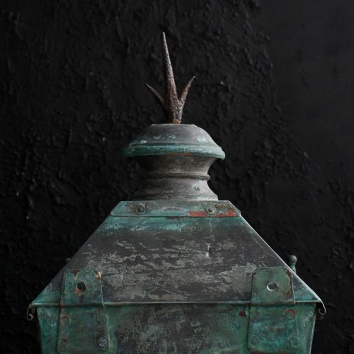 fig 6. A nineteenth-century copper wall lantern with glazed panels, a tapered rectangular body, and a decorative finial on top.
