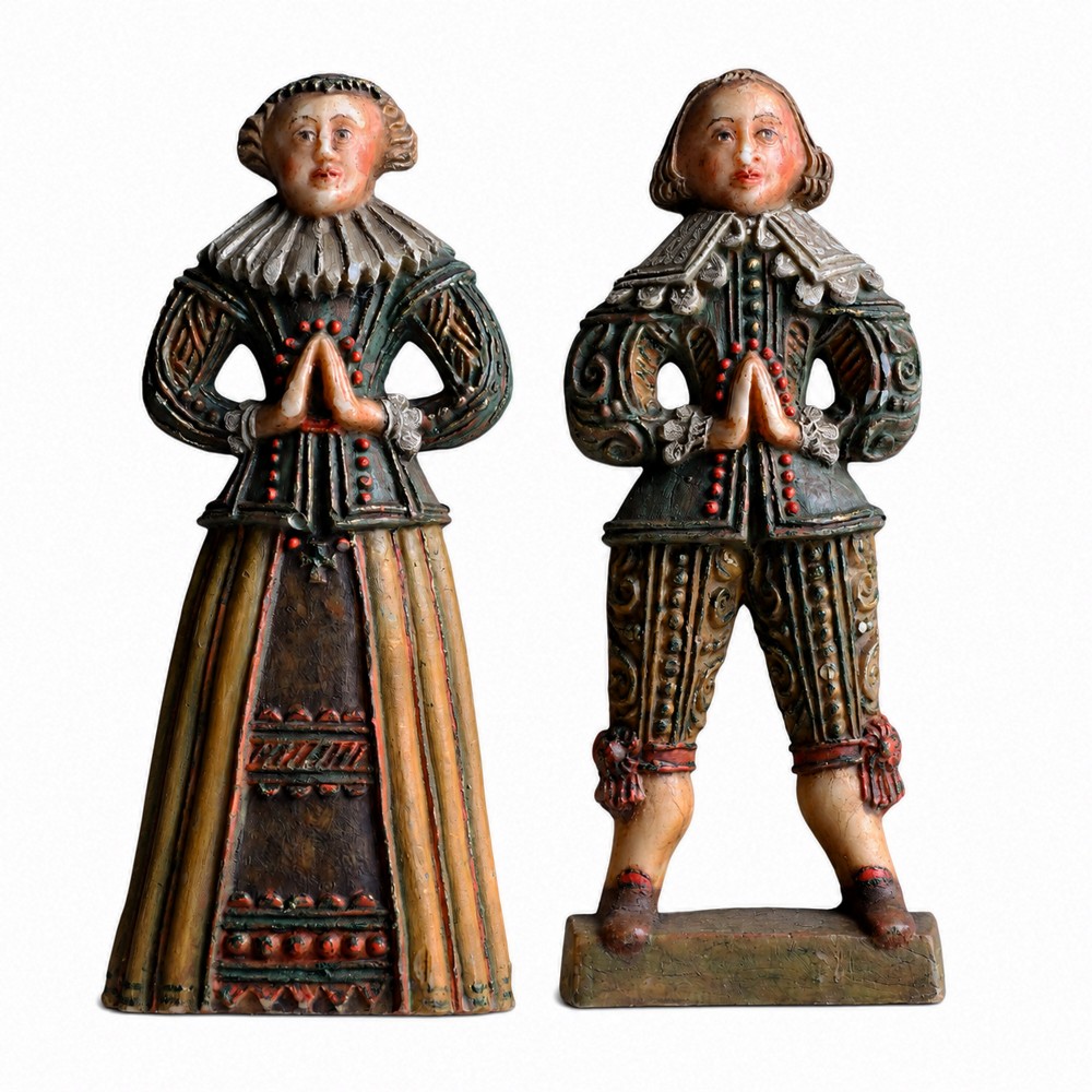 A pair of hand-carved polychrome wax figures depicting a man and a woman in 17th-century attire with hands clasped in prayer.