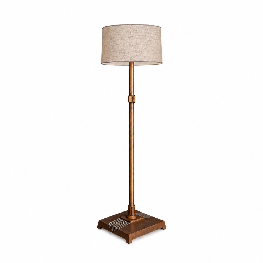 An Art Deco copper floor lamp featuring a square stepped base with geometric detailing, a slender central column, and a light beige linen drum shade.