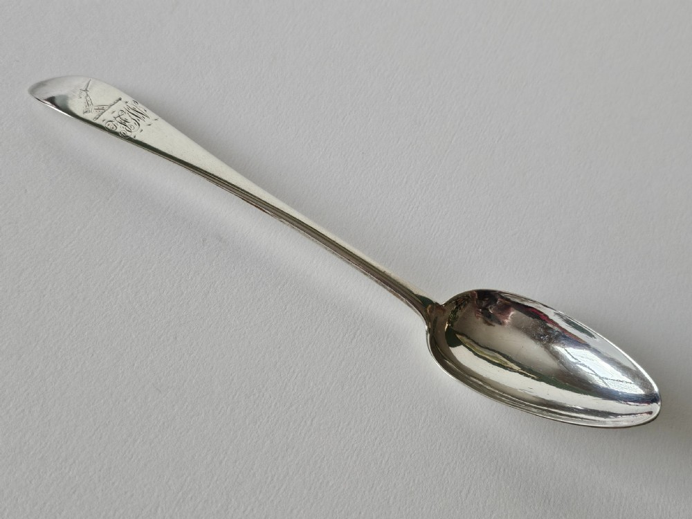 An antique Irish Georgian silver spoon featuring an elongated oval bowl and engraved detailing along the terminal.