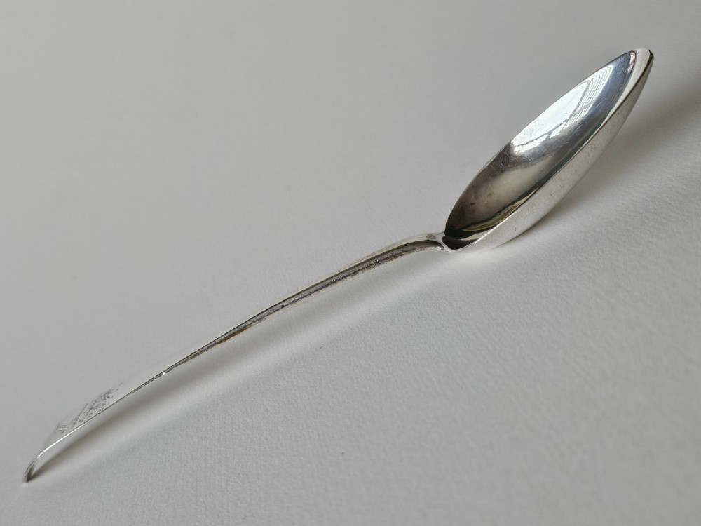 An antique Irish Georgian silver spoon featuring an elongated oval bowl and engraved detailing along the terminal. View VII