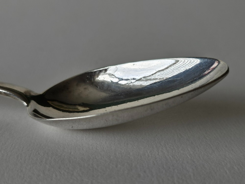 An antique Irish Georgian silver spoon featuring an elongated oval bowl and engraved detailing along the terminal. View VIII