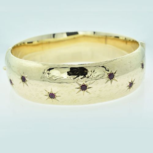 A wide 9ct yellow gold hinged bangle featuring star-set round rubies along a textured band.