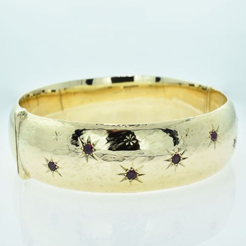fig 1. A wide 9ct yellow gold hinged bangle featuring star-set round rubies along a textured band.