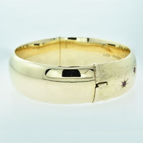 fig 3. A wide 9ct yellow gold hinged bangle featuring star-set round rubies along a textured band.