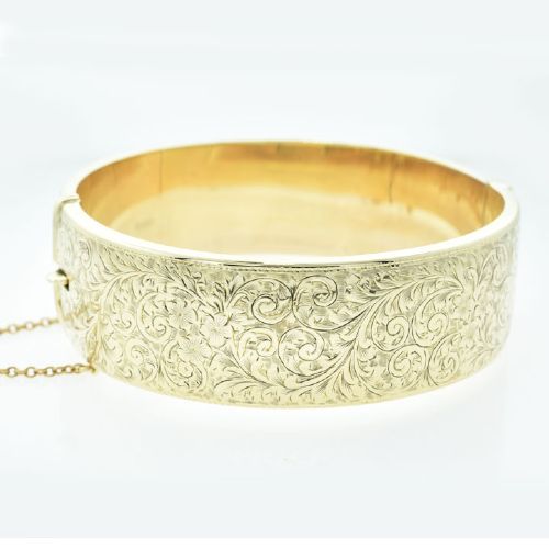 fig 1. A vintage 9ct yellow gold hinged bangle featuring detailed scroll engraving around the exterior band and an attached safety chain.