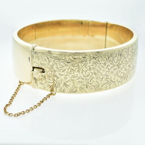 A vintage 9ct yellow gold hinged bangle featuring detailed scroll engraving around the exterior band and an attached safety chain. View IV
