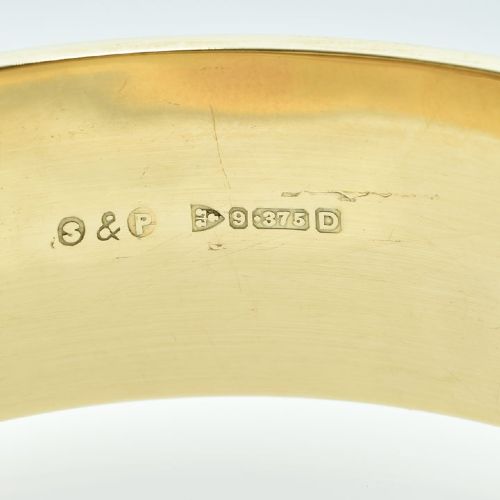 A vintage 9ct yellow gold hinged bangle featuring detailed scroll engraving around the exterior band and an attached safety chain. View VI