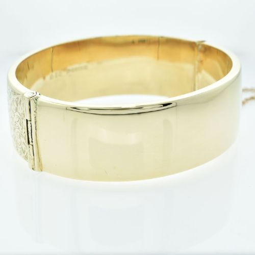 A vintage 9ct yellow gold hinged bangle featuring detailed scroll engraving around the exterior band and an attached safety chain. View VIII