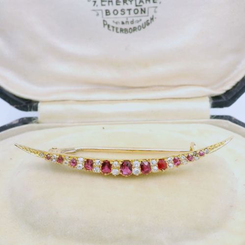 An antique late Victorian 15ct gold crescent brooch set with a graduated row of faceted red rubies and small white diamonds.