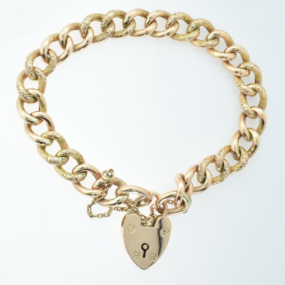 An antique rose gold curb link bracelet featuring alternating plain and engraved links fastened with a heart-shaped padlock clasp.