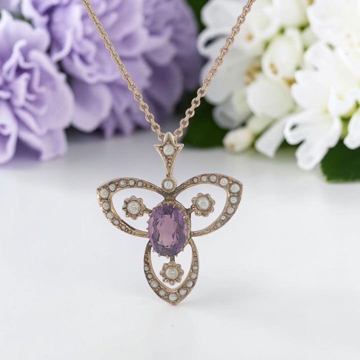 An Edwardian 9ct gold openwork pendant featuring a central oval amethyst surrounded by delicate seed pearls on a fine chain.