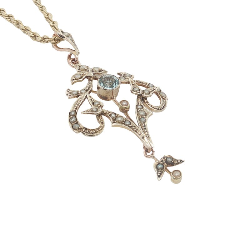 An openwork 9ct yellow gold Edwardian pendant set with a central round aquamarine and embellished with small seed pearls throughout. View IV