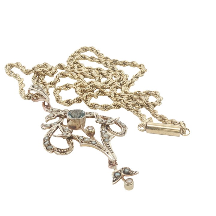 An openwork 9ct yellow gold Edwardian pendant set with a central round aquamarine and embellished with small seed pearls throughout. View VI