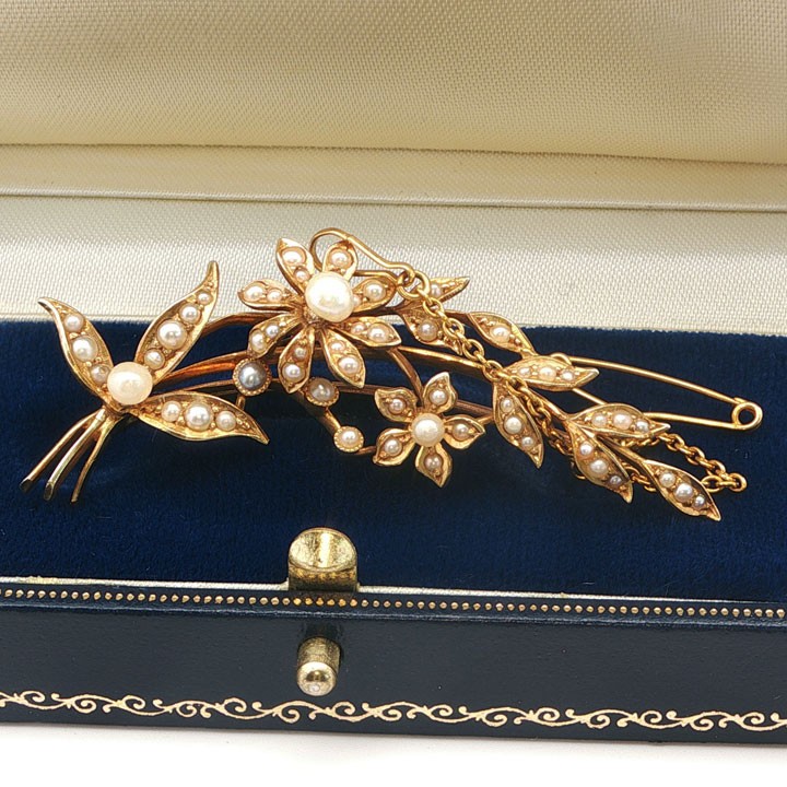 An antique 15ct yellow gold floral spray brooch featuring articulated flowers and leaves set with seed pearls, attached to a safety chain.