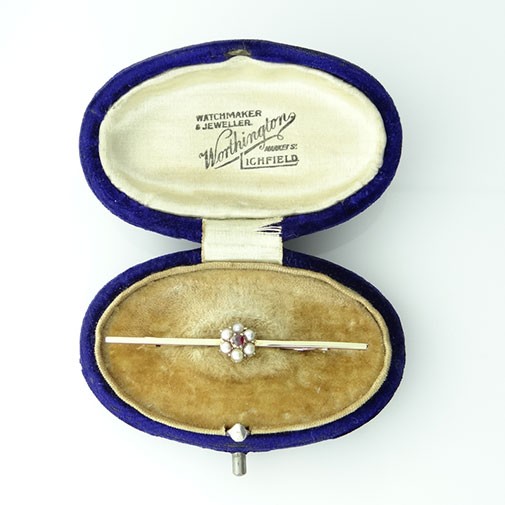 An antique yellow gold bar brooch featuring a central flower cluster set with a crimson almandine garnet and surrounding white seed pearls.