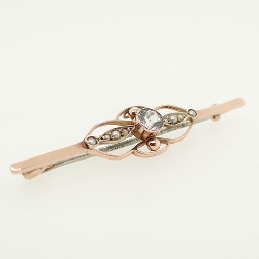 An antique 9ct rose gold bar brooch featuring a central circular aquamarine flanked by openwork wire motif panels inset with small seed pearls. View II