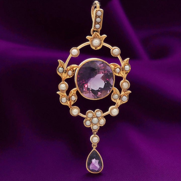 An openwork 15ct yellow gold oval pendant featuring a central round faceted amethyst framed by seed pearl leaf motifs, with a pear-cut amethyst drop suspended below. View II