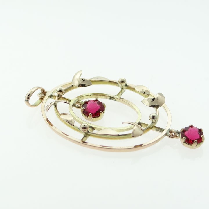 An oval 9ct yellow and rose gold openwork pendant featuring stylized leaf motifs and two round red simulated rubies. View II