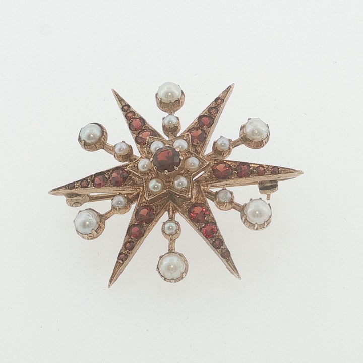 A 9ct yellow gold starburst brooch set with a central round garnet, surrounded by radiating point rays set with smaller garnets and seed pearls. View III