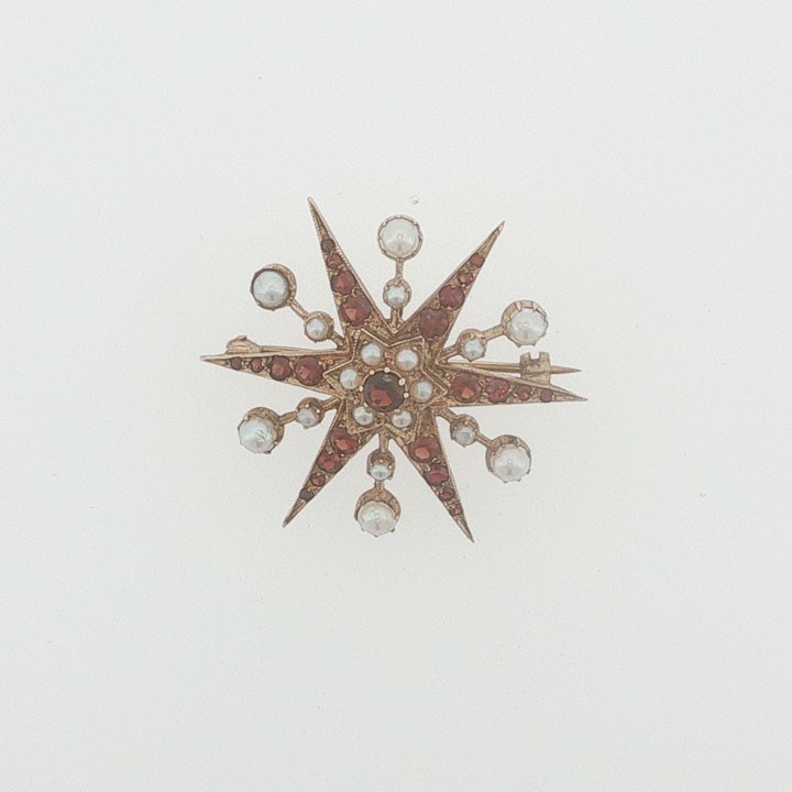 A 9ct yellow gold starburst brooch set with a central round garnet, surrounded by radiating point rays set with smaller garnets and seed pearls. View IV