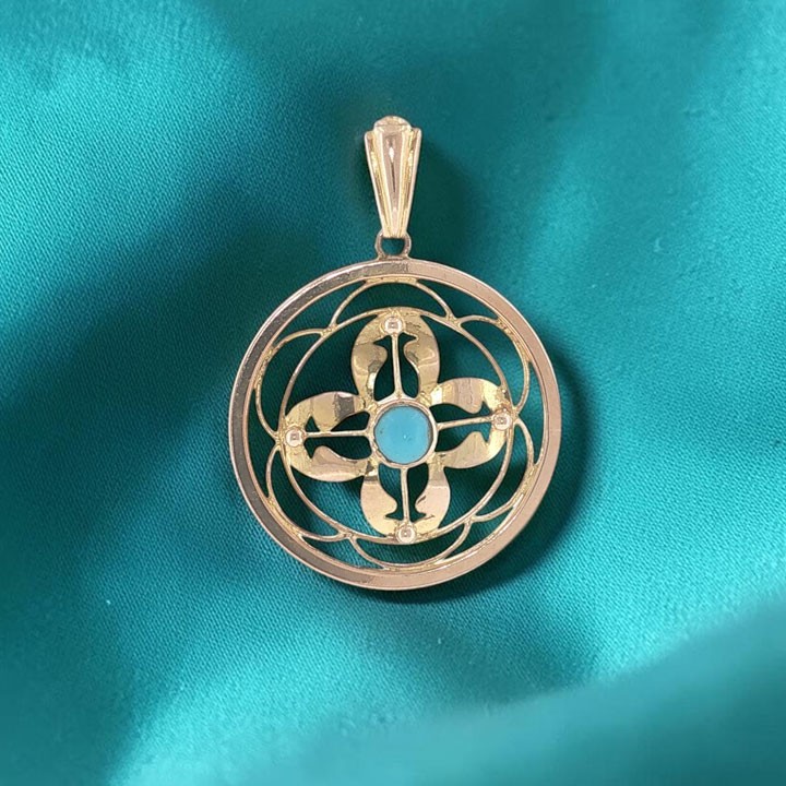 A circular 9ct yellow gold openwork pendant set with a round central turquoise cabochon framed by floral scrollwork.