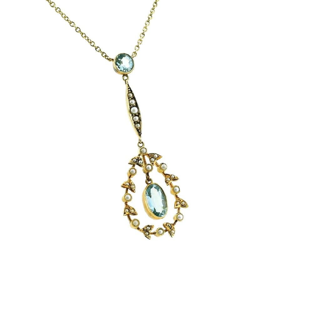 An Edwardian 15ct gold lavalier necklace featuring a round aquamarine top stone, a seed-pearl-set vertical bar, and a floral garland pendant surrounding a suspended oval aquamarine. View V