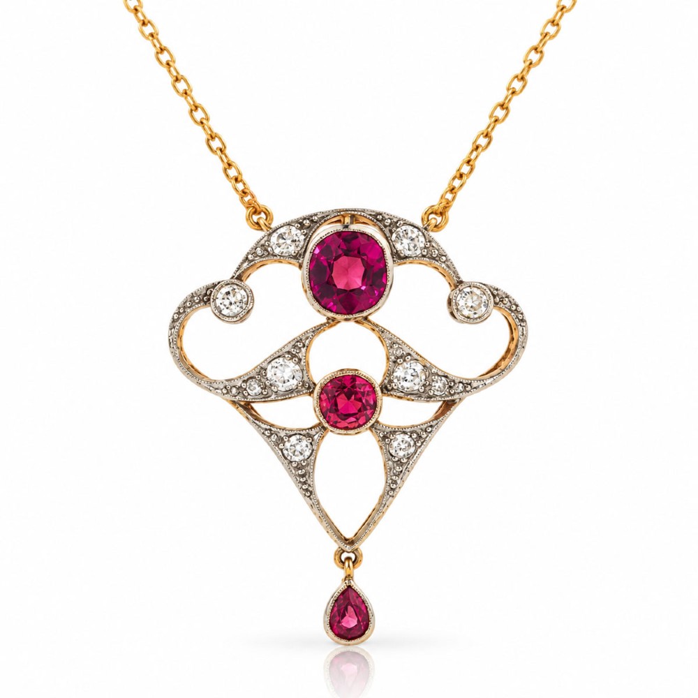 An Edwardian openwork 15ct gold and silver-topped pendant set with round rubies, diamond accents, and a pear-cut ruby drop on a gold chain.