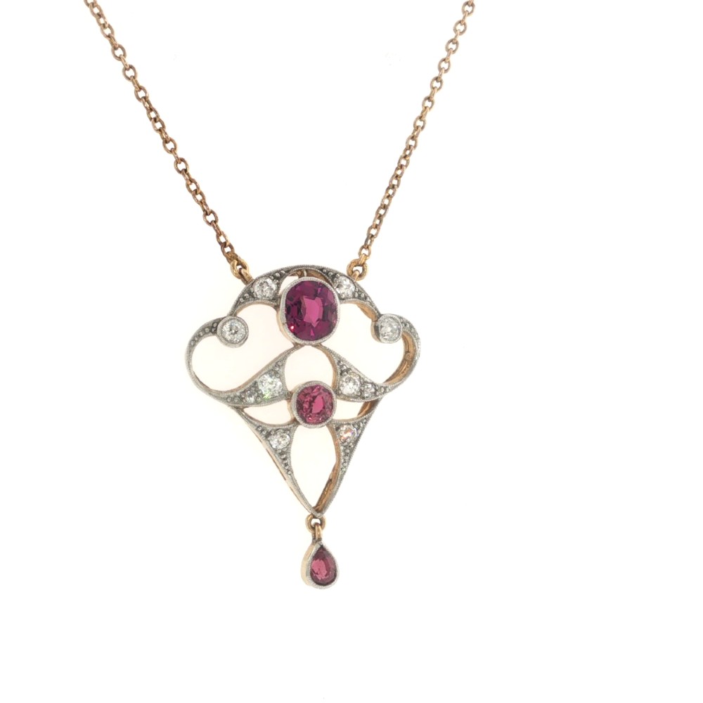 An Edwardian openwork 15ct gold and silver-topped pendant set with round rubies, diamond accents, and a pear-cut ruby drop on a gold chain. View IV