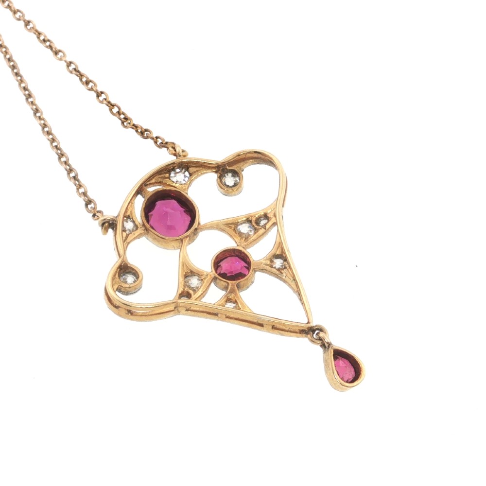 An Edwardian openwork 15ct gold and silver-topped pendant set with round rubies, diamond accents, and a pear-cut ruby drop on a gold chain. View VI