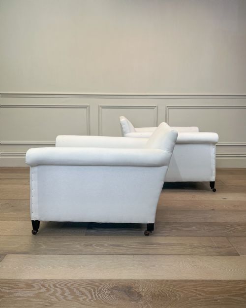 fig 1. A pair of late nineteenth-century armchairs upholstered in white fabric featuring scroll arms, detail studding, and dark wooden legs with brass castors.