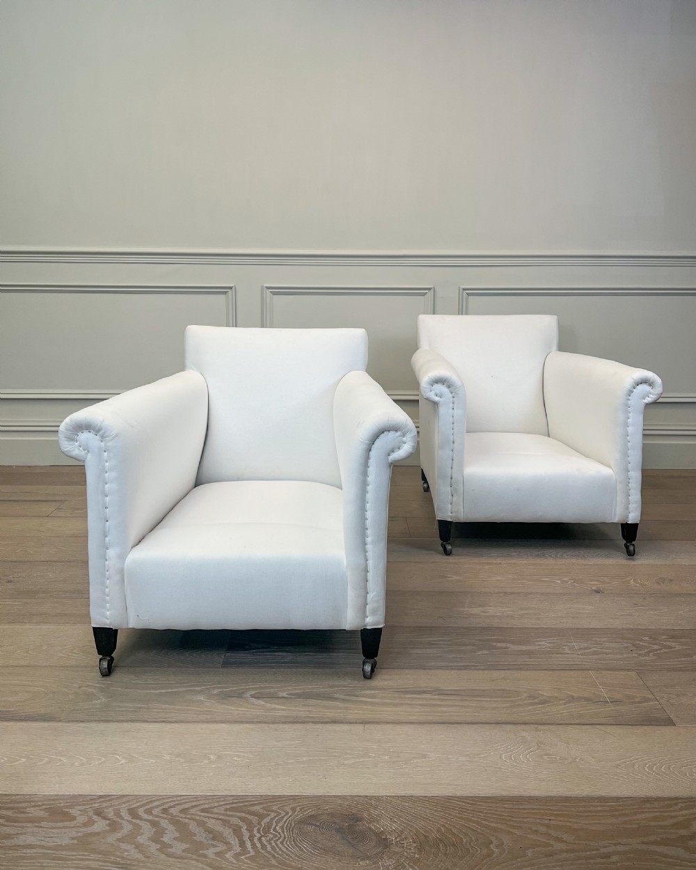 A pair of late nineteenth-century armchairs upholstered in white fabric featuring scroll arms, detail studding, and dark wooden legs with brass castors. View III